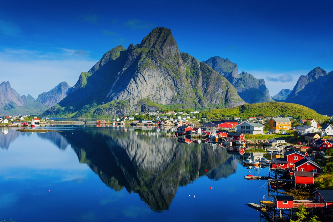 Malerische Fjordlandschaft mit Bergen und bunten Häusern, reflektiert im Wasser.